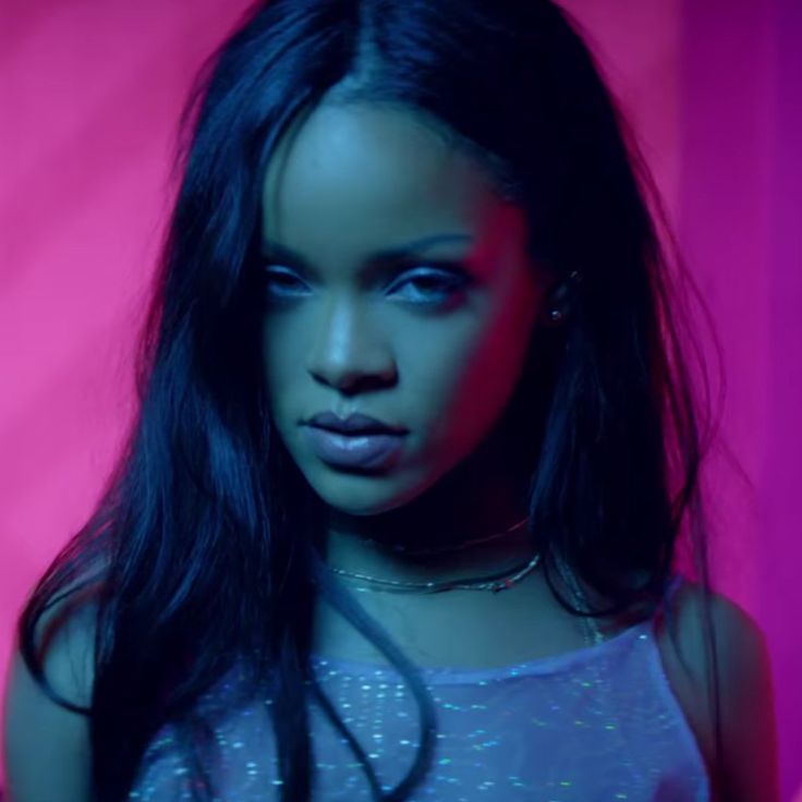 a woman with long black hair standing in front of a pink background wearing a silver top