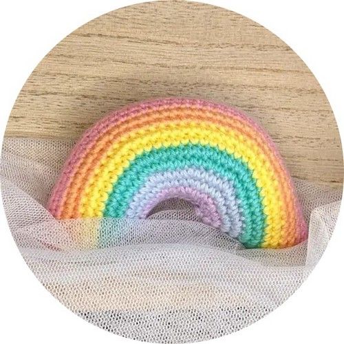 a crocheted rainbow sitting on top of a wooden table next to a white net