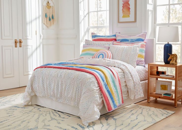 a bed with colorful comforters and pillows in a room next to a window on a rug