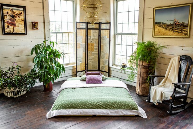 a bed sitting in a bedroom next to two windows with potted plants on them