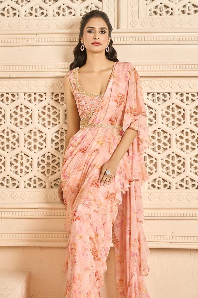 Peach pre-stitched saree with all-over floral prints and ruffle palla. Comes with printed, padded and embellished blouse. Paired with an embellished belt.
Components: 3
Pattern: Printed, Embellished
Type Of Work: Floral Patterns
Neckline: Scoop
Sleeve Type: Sleeveless
Fabric: Saree: Chiffon, Blouse: Georgette
Color: Peach
Other Details: 
Scalloped hem blouse
Ruffled saree
Blouse closure: Side zipper
Occasion: Destination Wedding - Aza Fashions Ruffle Saree Blouse, Coral Saree, Flower Print Gown, Ruffled Saree, Saree Chiffon, Ruffle Sarees, Stitched Saree, Peach Saree, Indian Outfits Lehenga