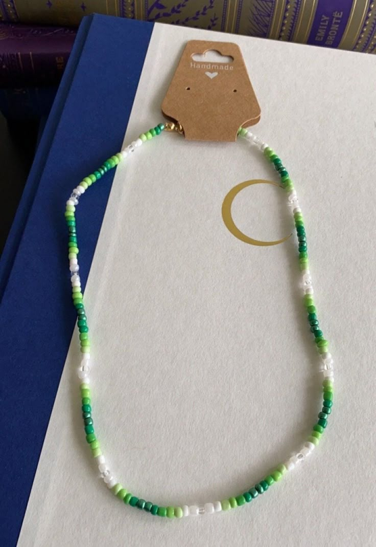 a green and white beaded necklace sitting on top of a blue binder next to a book