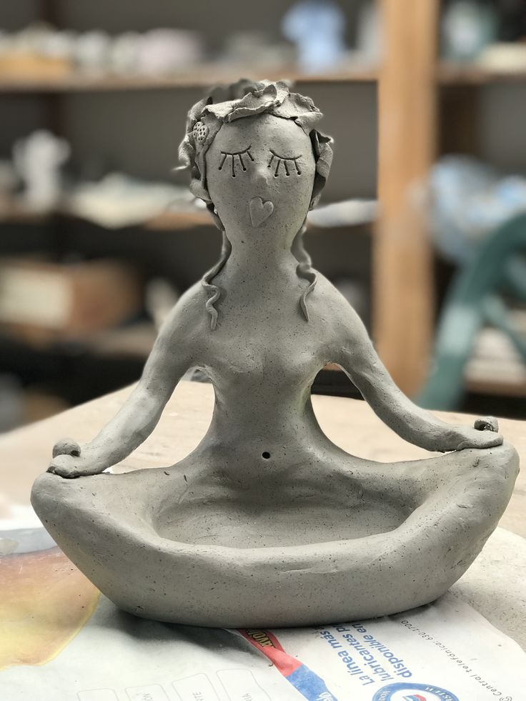 a statue of a woman sitting in a lotus position on top of a table next to shelves