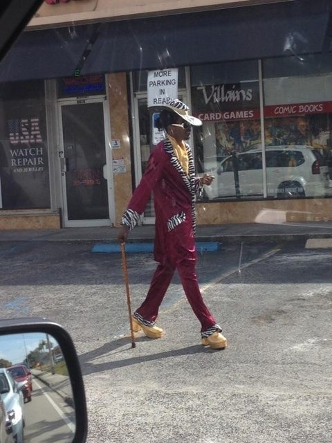 a man in a clown suit walking down the street with a cane and hat on