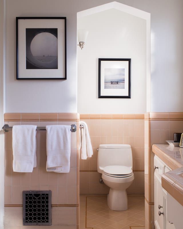 a white toilet sitting next to a bathroom sink under a framed picture on the wall