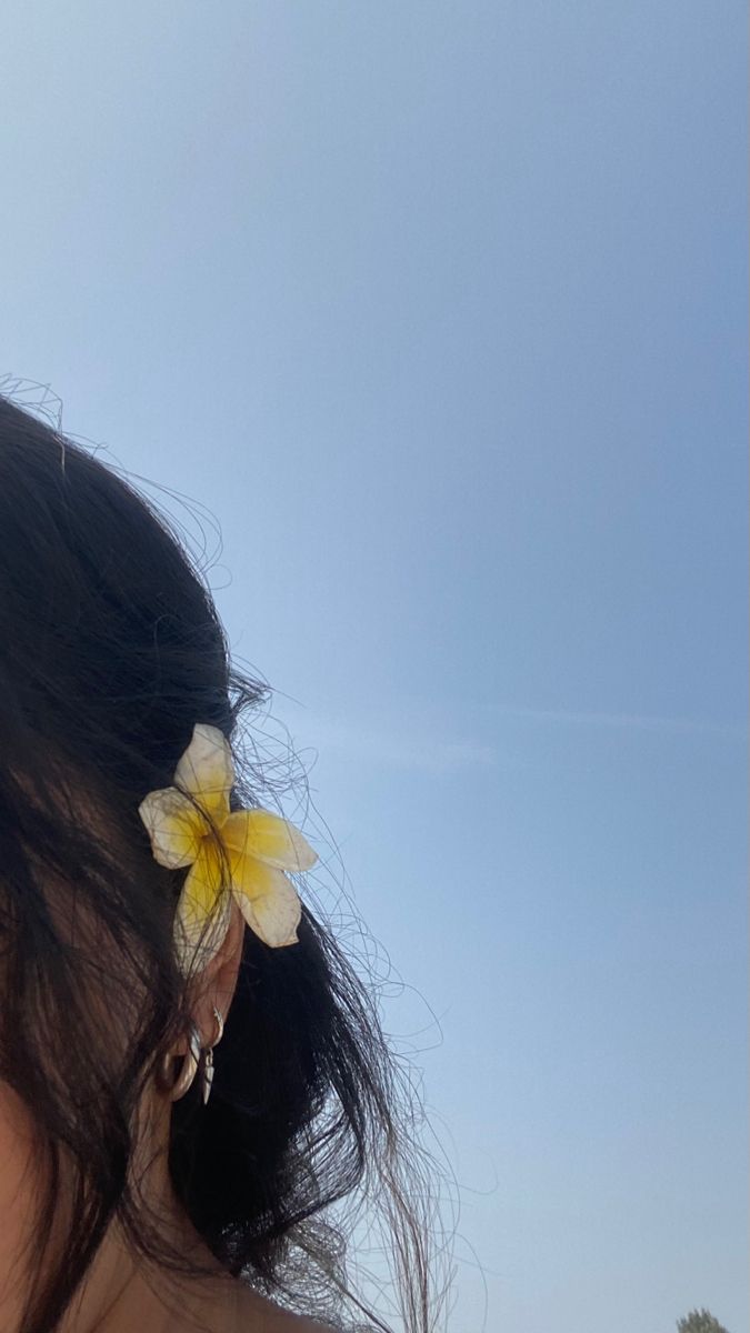 a woman with a flower in her hair standing on the beach looking at the ocean