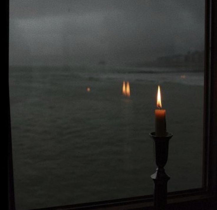 a candle is lit in front of a window overlooking the water and foggy sky