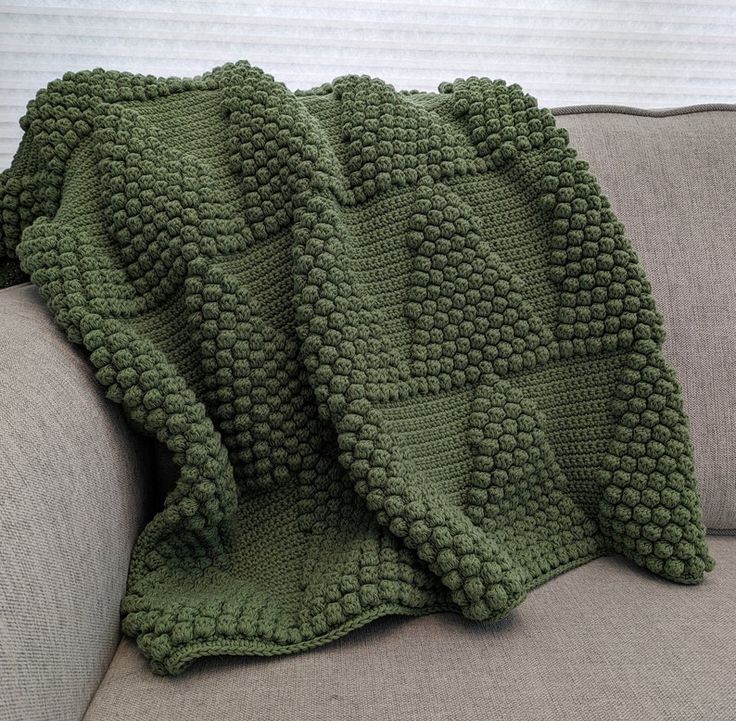 a green crocheted blanket sitting on top of a couch next to a pillow