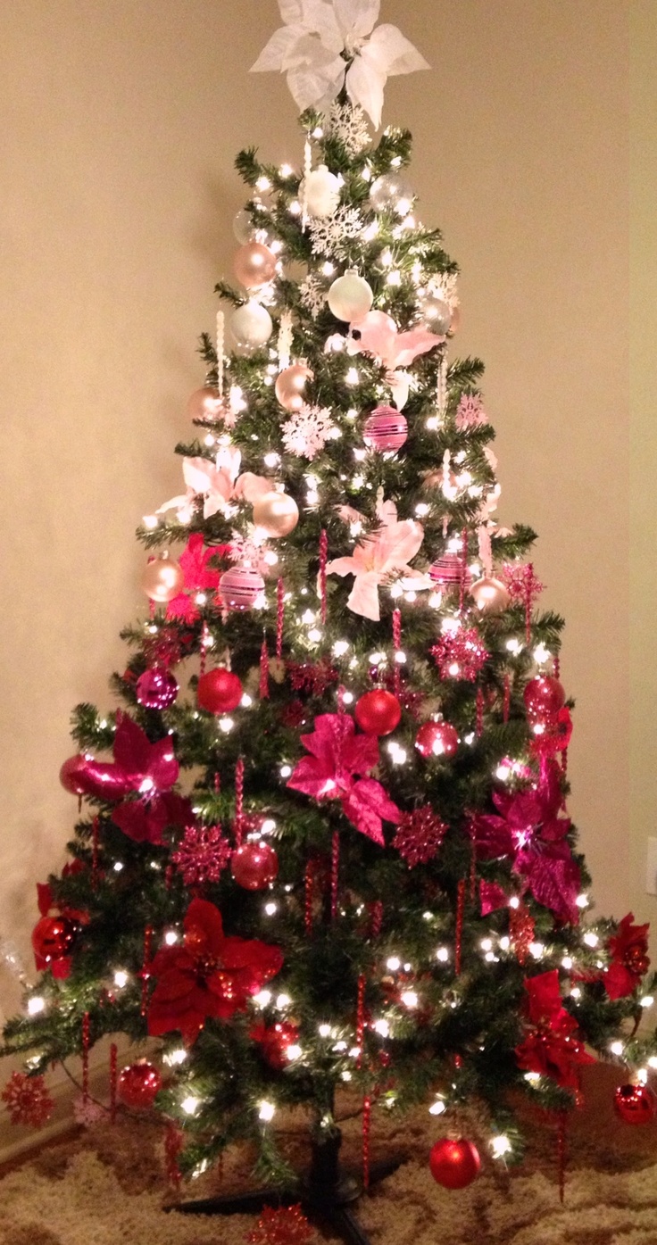 a decorated christmas tree with pink and red ornaments on it's branches, lights and bows