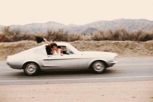 a woman sitting in the driver's seat of a white car with mountains in the background