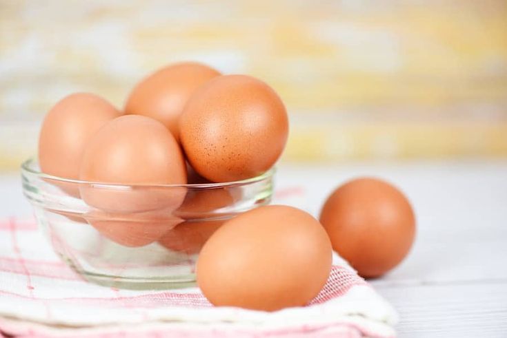 a glass bowl filled with brown eggs on top of a white and pink towel,