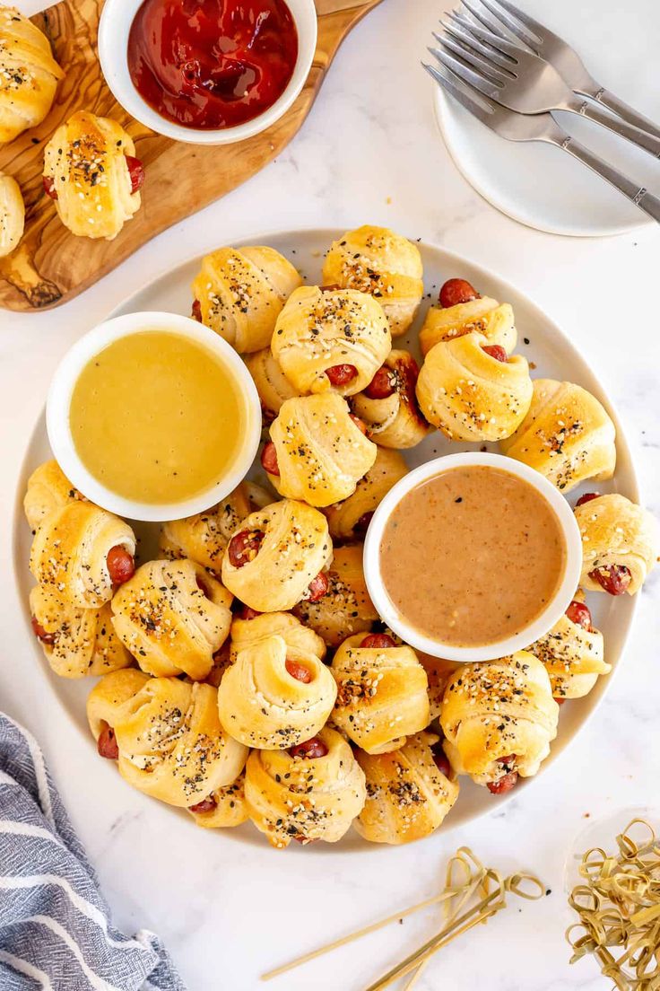 a white plate topped with pigs in a blanket and dipping sauce next to silverware