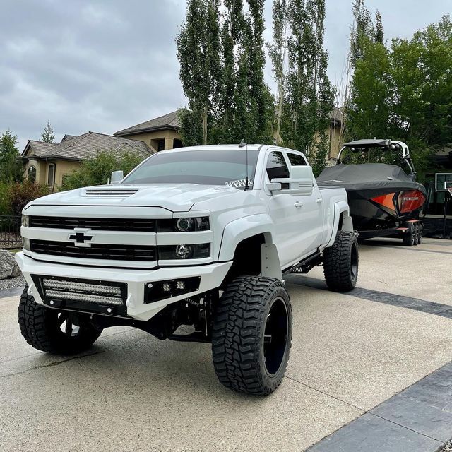 a white truck parked in front of a boat on the street next to a house