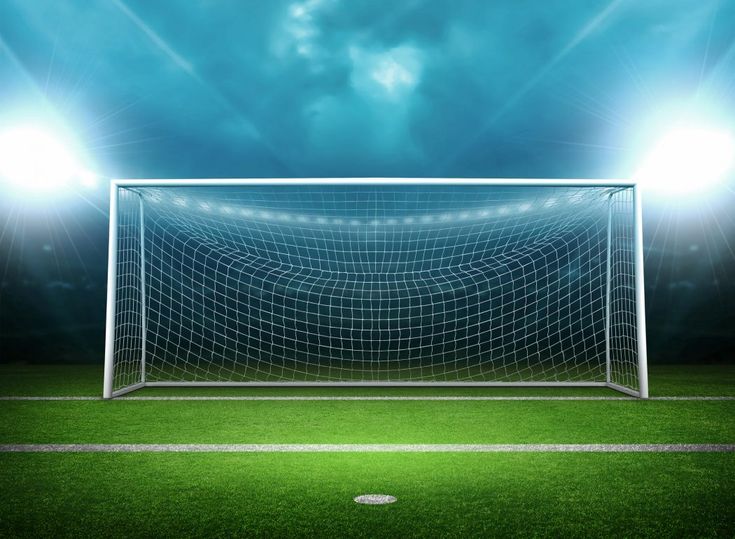 a soccer goal on an empty field with flood lights in the background at night time