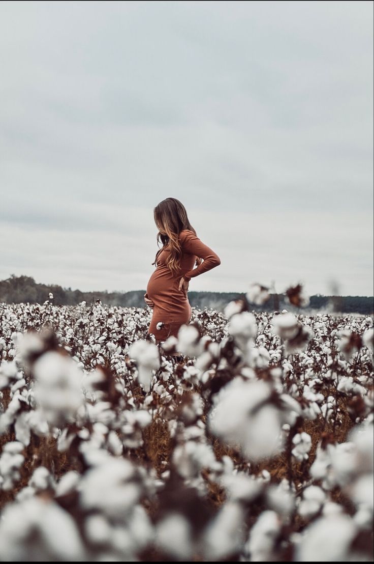 a woman standing in a cotton field with her back to the camera and looking into the distance