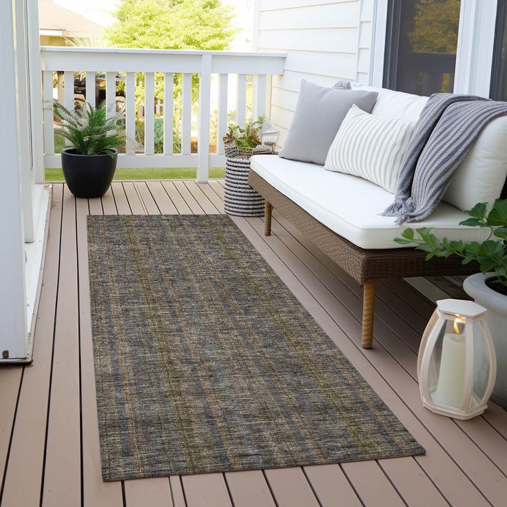 a porch with a couch and rug on the floor next to a potted plant