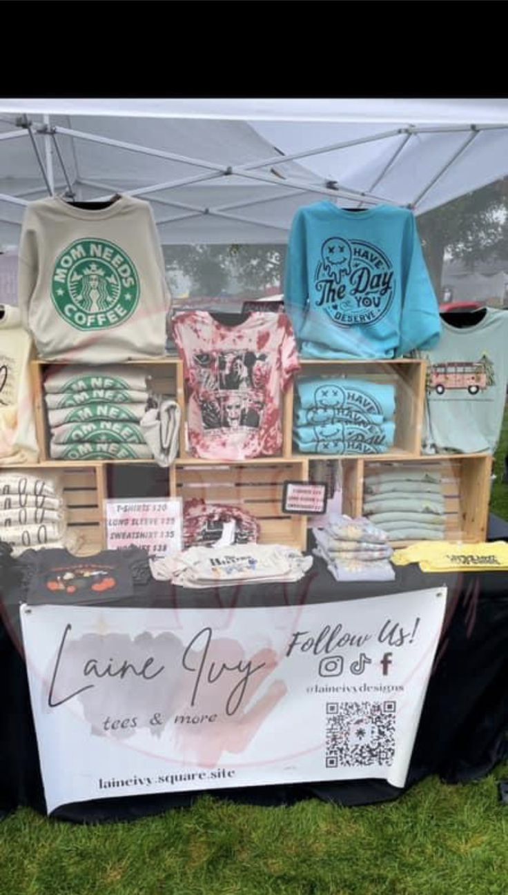 a booth selling t - shirts and other items at an outdoor event in the grass