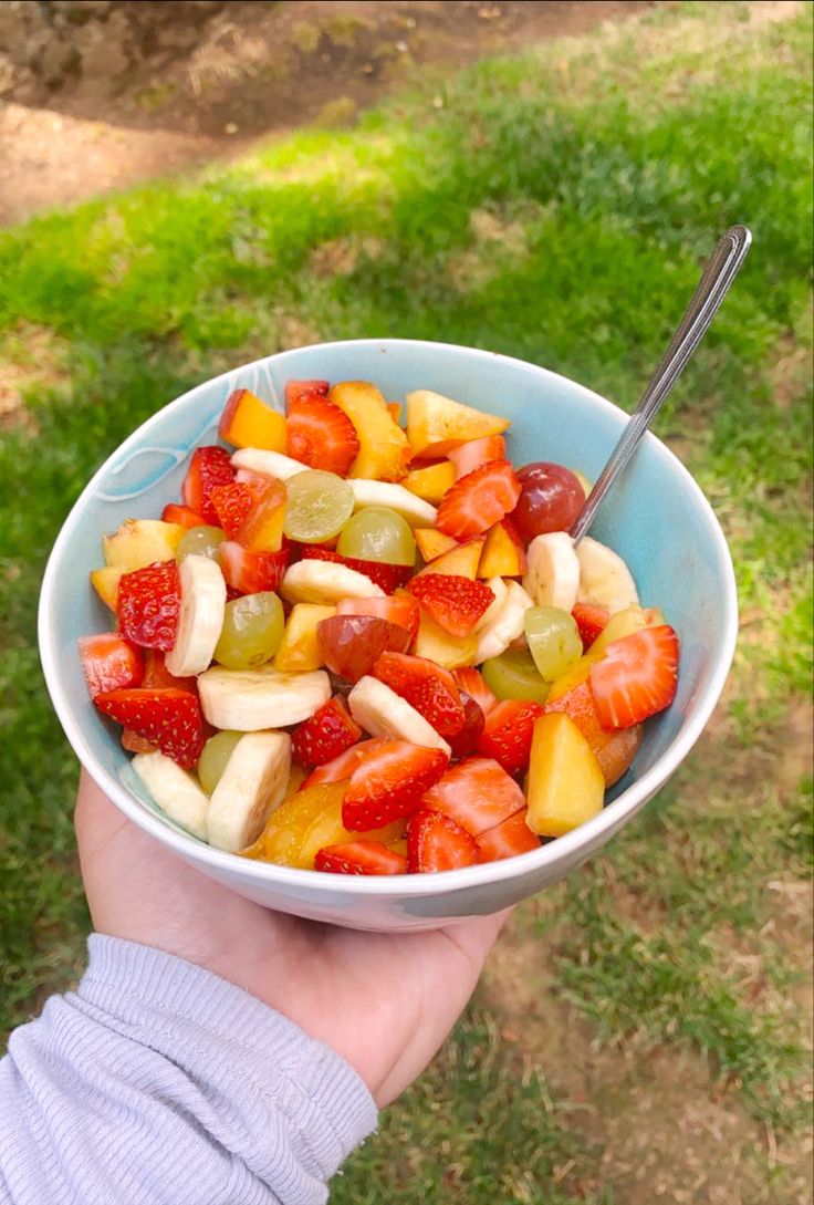 a person is holding a bowl of fruit in their left hand and the other hand has a spoon in it