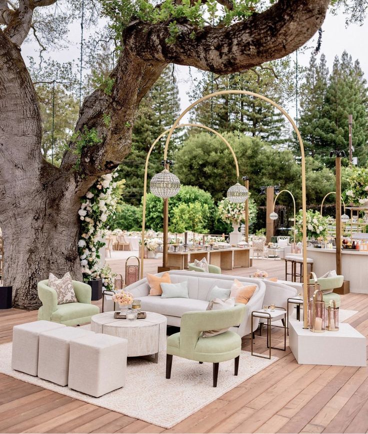 an outdoor seating area with chairs and tables under a large tree in the middle of a wooden deck