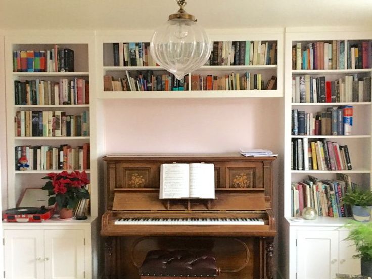 an old piano sits in front of bookshelves with many books on it and a chandelier hanging from the ceiling