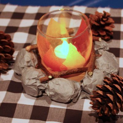 a lit candle sits in a glass bowl on a checkered tablecloth with pine cones