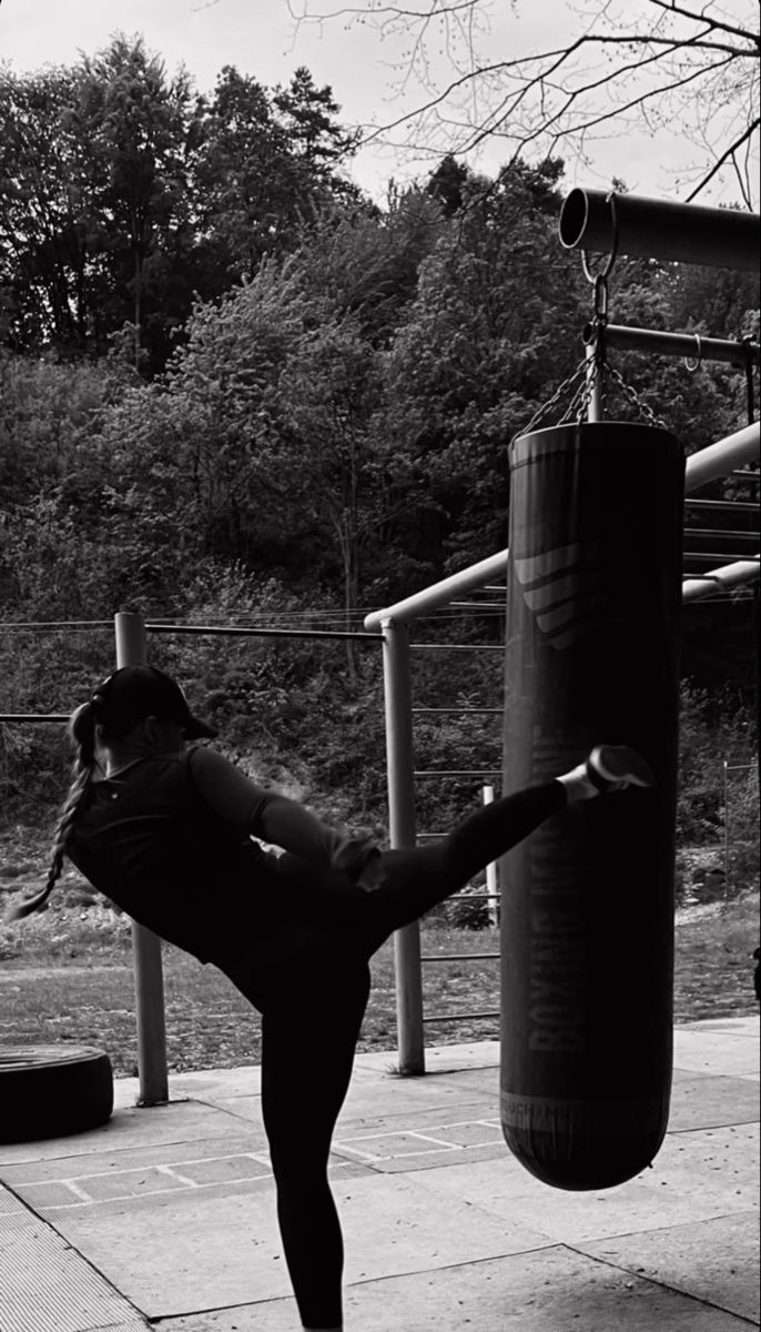 a woman is practicing her kickbox moves on the sidewalk near a punching bag in black and white