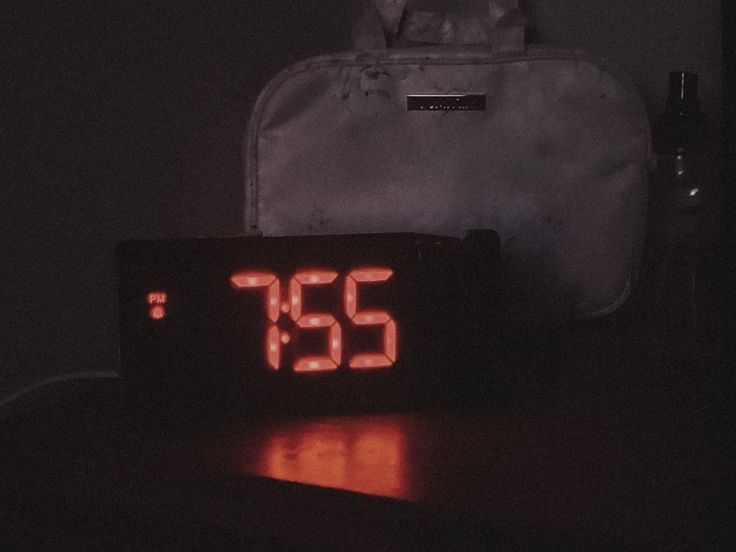 an alarm clock sitting on top of a table next to a white bag and pen