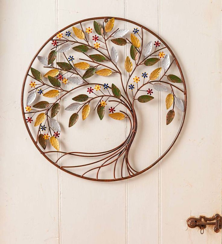 a metal tree with leaves and flowers on a white wall next to a door handle