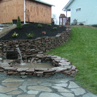 a stone patio with a fire hydrant in the center surrounded by grass and rocks