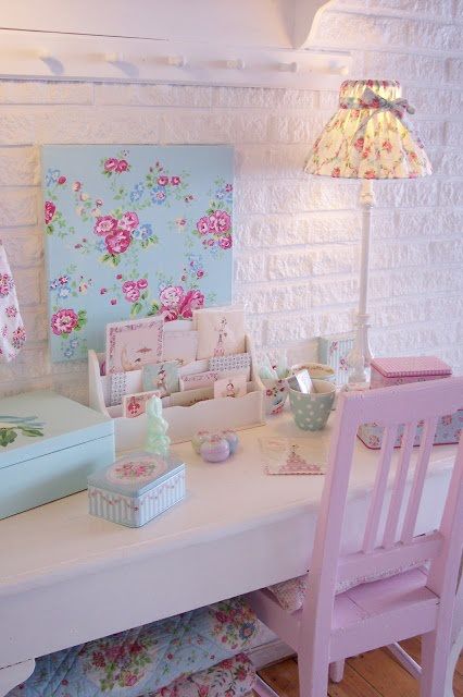 a white desk topped with lots of pink and blue items next to a wall covered in flowers