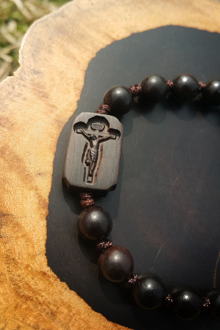 +. This is a Wooden Rosary Bracelet. +.It is knotted bracelet and it is adjustable . +.The crufix is carved in elevorate and three dementional shape. +.+.+.+.+. Materials +.+.+.+.+.+. Cross: Mpingo(Africa black wood) Beads : ebony 8mm +.+.+.+.+. Size +.+.+.+.+. Cross : 13.3mm(Width) *20mm(Height) Beads: 8mm +. Engraved characters(e.g. baptismal name, name,etc) on back side. please send characters that you want. Please let me know by message. It's Free engraving +.Wood is a natural Product. Pleas Spiritual Brown Rosary Bracelet For Gift, Handmade Cross-shaped Rosary Bracelet For Blessing, Handmade Cross Rosary Bracelet For Blessing, Spiritual Rosary Bracelet With Cross Shape, Spiritual Cross Rosary Bracelet Gift, Spiritual Cross Rosary Bracelet For Gift, Spiritual Gift Rosary Bracelet With Cross, Wooden Beads Rosary With Crucifix As Gift, Gift Rosary With Wooden Beads And Crucifix