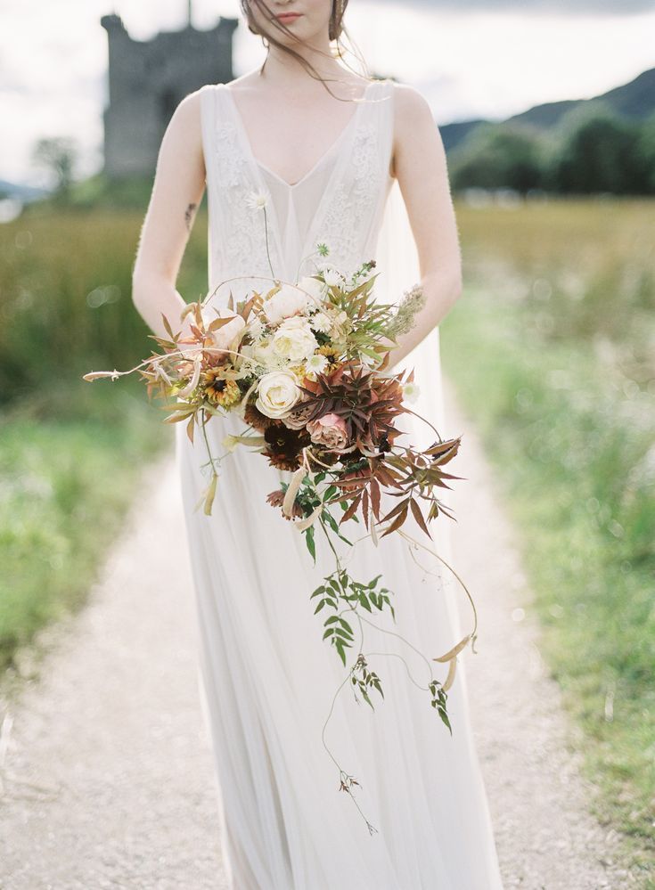 a woman in a long white dress holding a bouquet on the side of a road