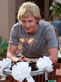 a man sitting at a table with a cake and sparklers in the air above it