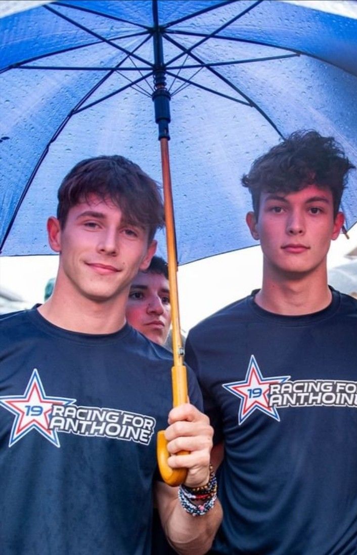 two young men standing under an umbrella in front of a group of people wearing t - shirts