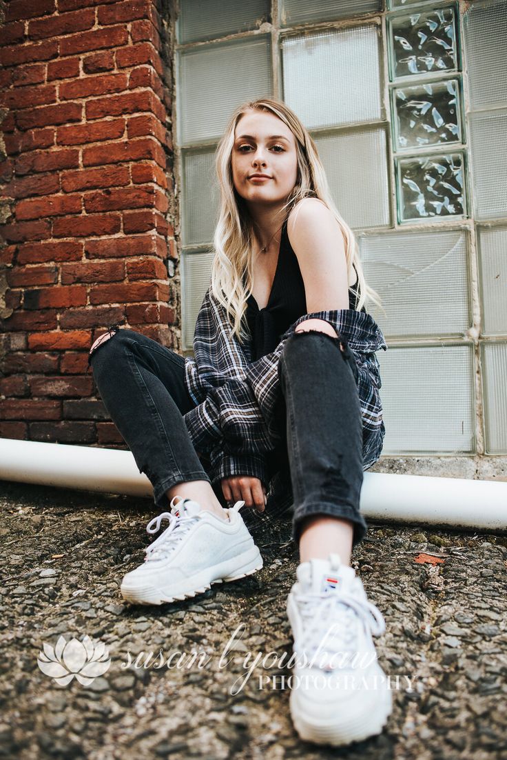 a woman sitting on the ground with her legs crossed wearing white sneakers and ripped jeans