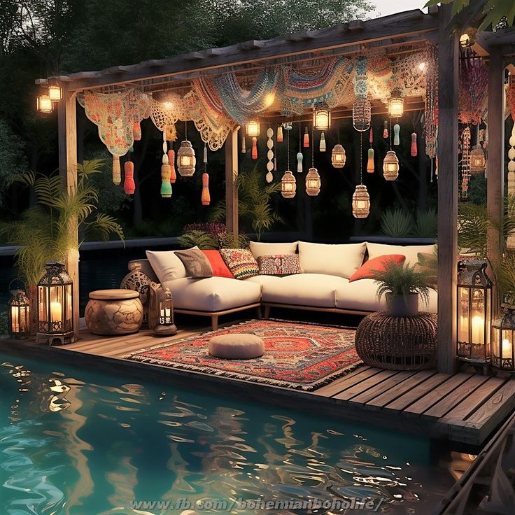 an outdoor living area next to a pool with lights hanging from the ceiling and pillows on the floor