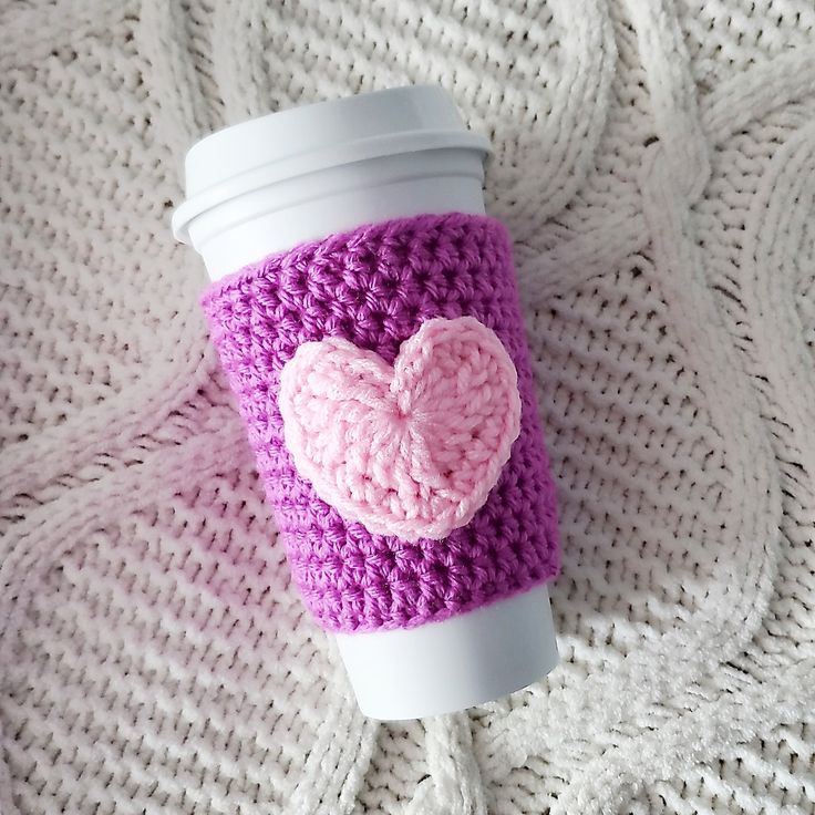 a coffee cup with a crocheted heart on the lid sitting on a blanket