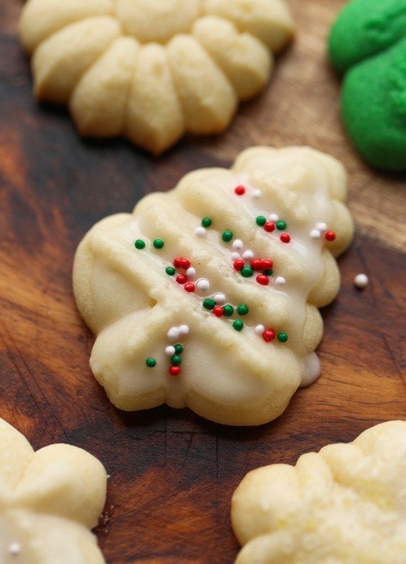 some cookies with sprinkles on top of a wooden cutting board next to green cookies