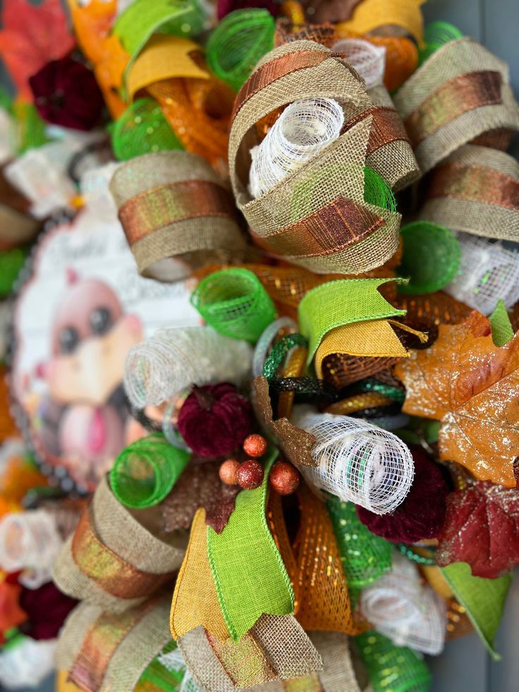 a close up of a wreath on a door with fall leaves and ribbons around it