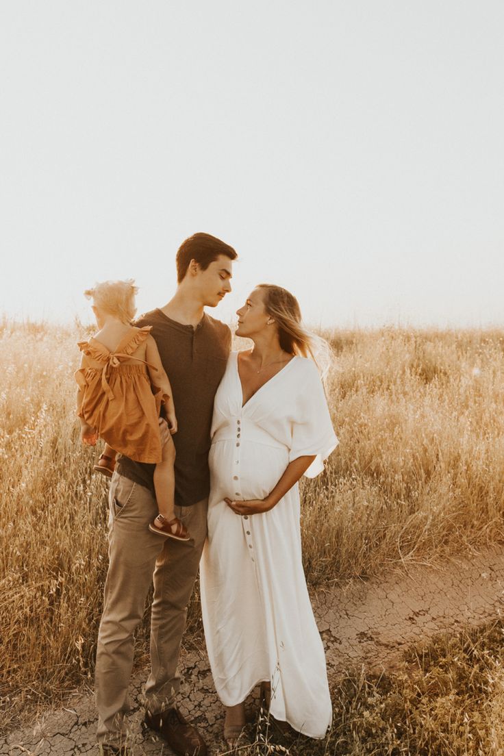 a man and woman holding a baby standing in the middle of a field