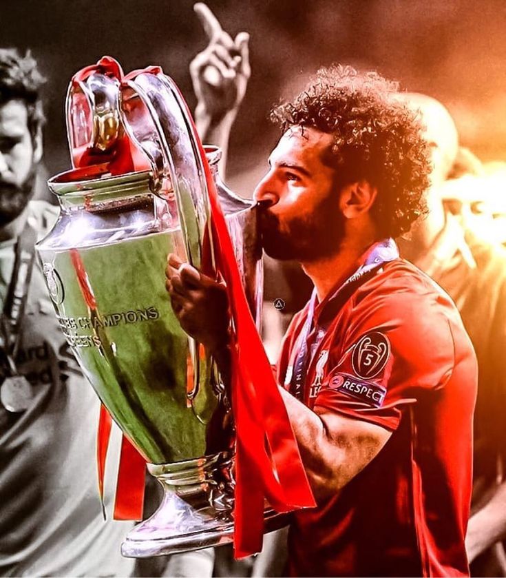 a man holding a trophy in front of his face and pointing to the sidelines