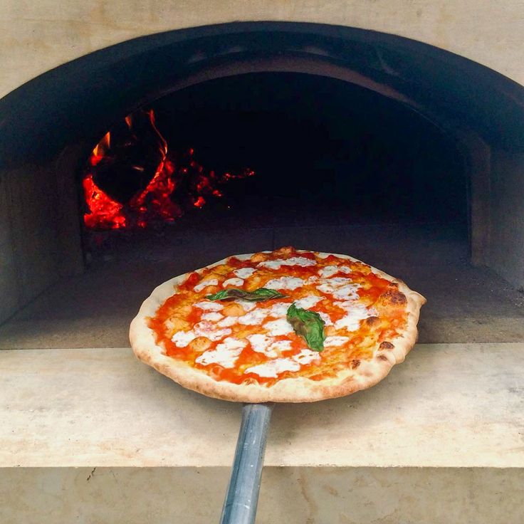 a pizza sitting in front of an open brick oven with the door ajar to it