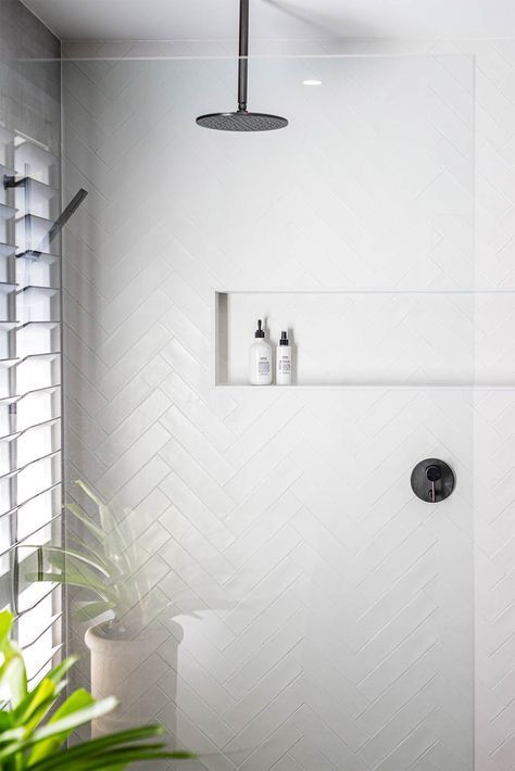 a bathroom with a shower head and white tiles on the wall, next to a plant