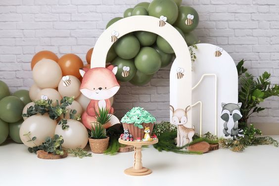 a table topped with lots of balloons and animals next to a cake stand filled with cupcakes