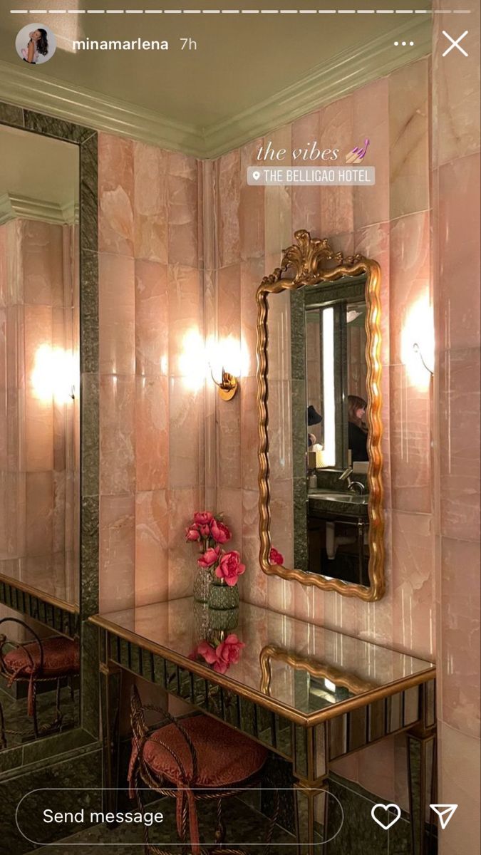 a mirror and vanity in a room with pink flowers on the table next to it