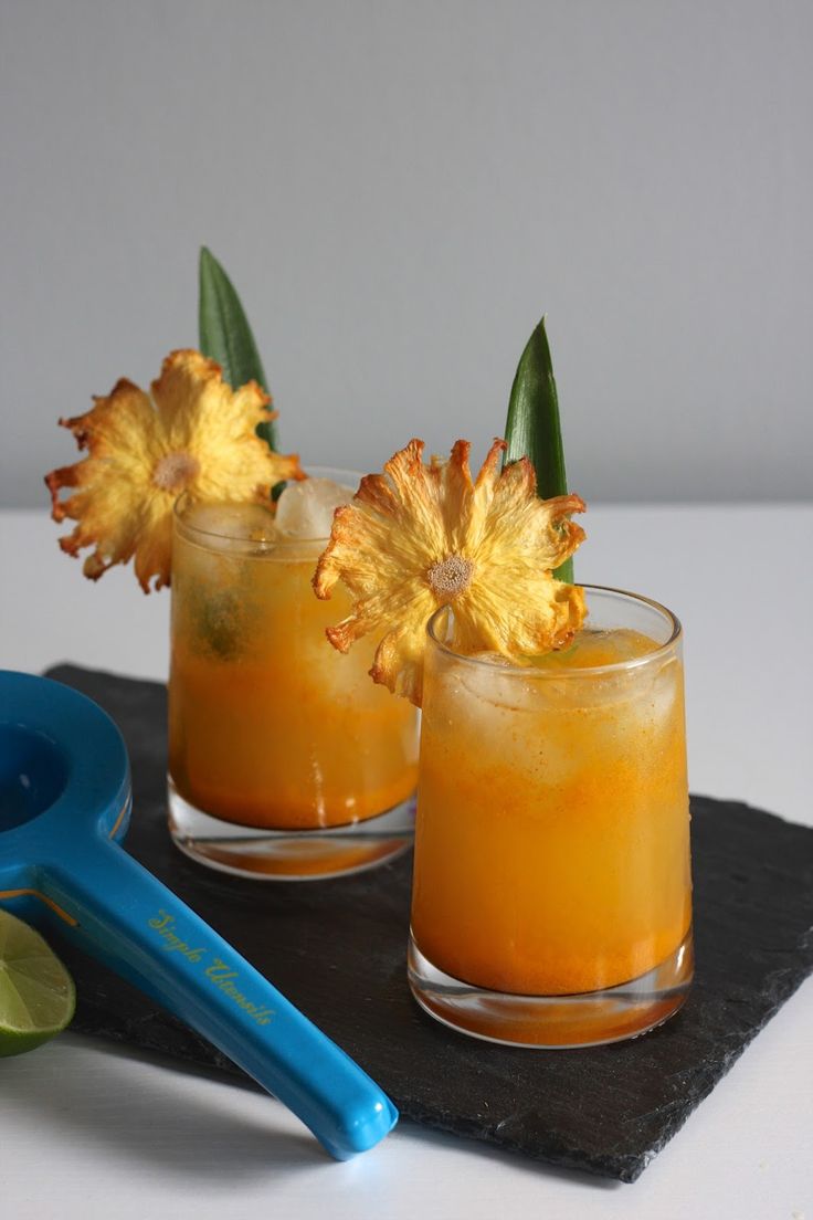 two glasses filled with orange juice and garnished with flowers on a black tray