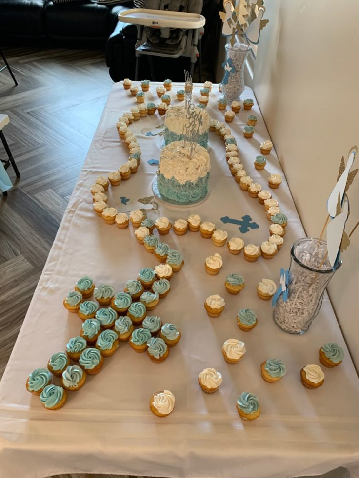 a table topped with lots of cupcakes covered in frosting next to a cake