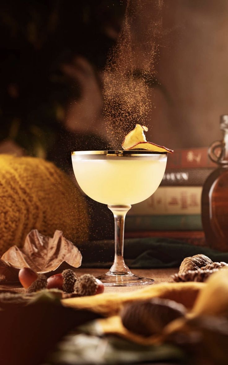 a glass filled with an alcoholic drink on top of a table next to some books