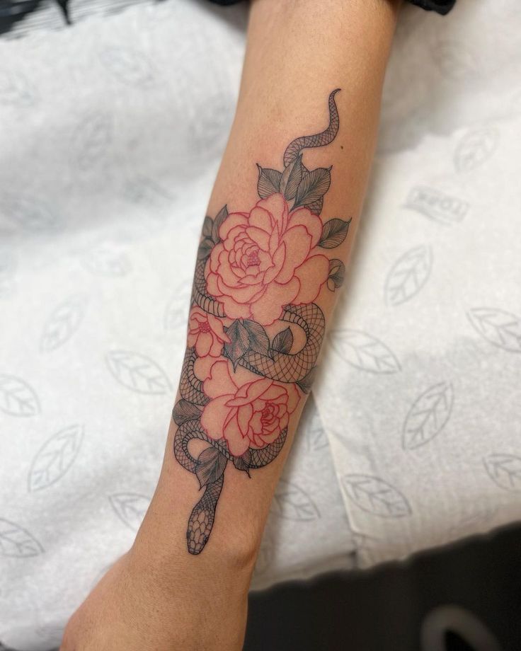 a woman's arm with a snake and rose tattoo on her left arm, sitting on a bed