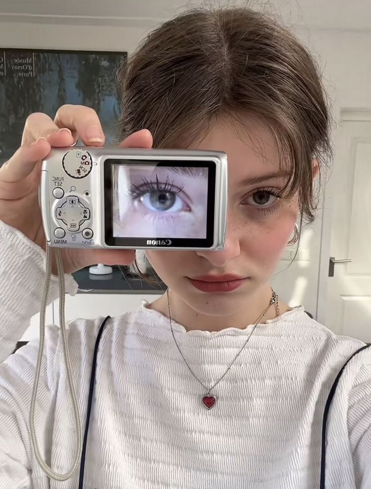 a young woman holding up a camera to take a selfie with her eye open